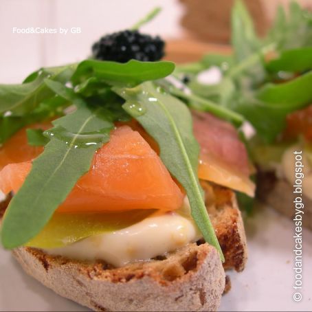 Crostini de pan rústico con salmón ahumado, pepinillos y rúcula.