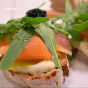 Crostini de pan rústico con salmón ahumado, pepinillos y rúcula.