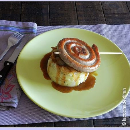 Piruleta de salchicha de ternera sobre timbal de patata y cebolla caramelizada